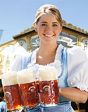 Woman at Oktoberfest in traditional outfit while holding three full beer mugs